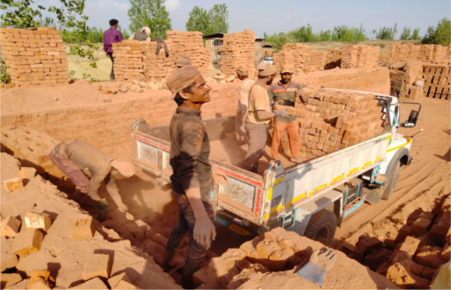 Migrant labourers load bricks on a truck at a brick kiln.